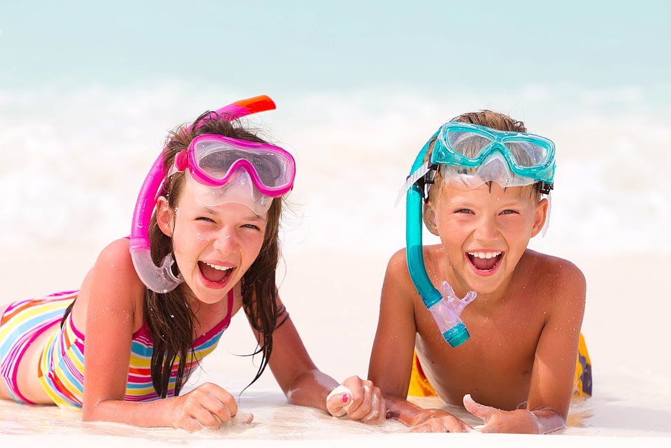 girl and boy wearing snorkels while stomach lying on white sand HD wallpaper